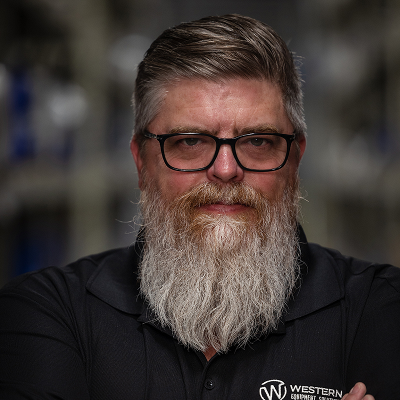 Craig Berninger, Sales Manager, standing in a warehouse with beard and glasses.