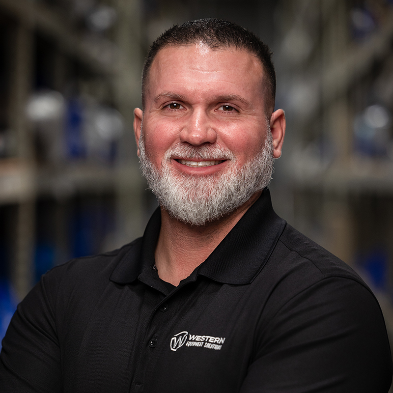 Portrait of John Wilson, Chief Executive Officer, wearing a black shirt and sporting a beard.