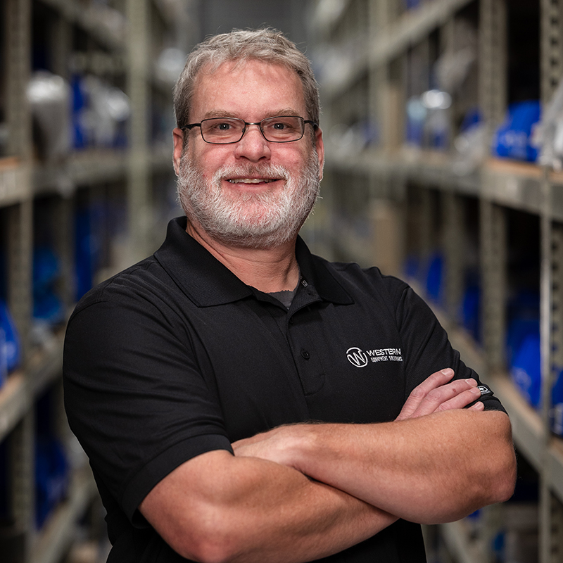 Matt Wilson, the Parts Manager, stands in a warehouse, donning glasses and a beard. His presence exudes confidence and professionalism