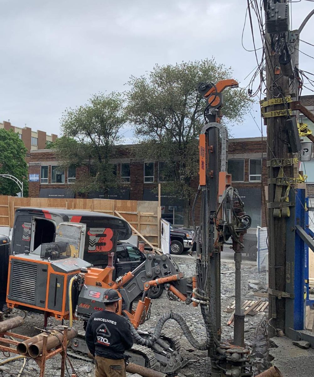 Construction worker in orange safety gear operating machine at construction site.